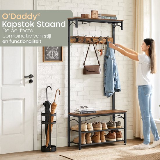 Vrouw hangt jas op aan bruine houten kapstok met zwarte haken, schoenenrek en paraplubak.