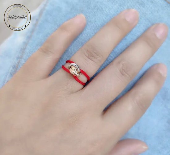 Gouden ring met twee lussen op een rode draad, gedragen op de middelvinger.