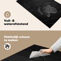 Een hand veegt met een grijze doek over de zwarte inductiebeschermer met geometrisch patroon. Waterdruppels zijn zichtbaar op het oppervlak.
