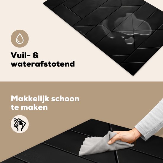 Een hand veegt met een grijze doek over de zwarte inductiebeschermer met geometrisch patroon. Waterdruppels zijn zichtbaar op het oppervlak.
