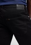 Close-up van de achterkant van een zwarte jeans met Lee logo.