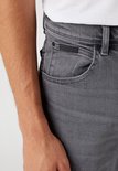 Close-up van de grijze jeans met een zwart label rechts op de tailleband.