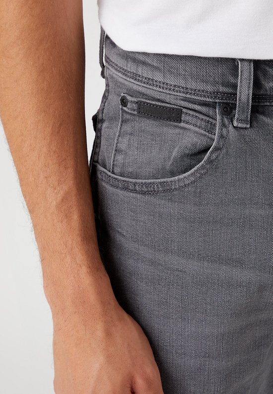 Close-up van de grijze jeans met een zwart label rechts op de tailleband.