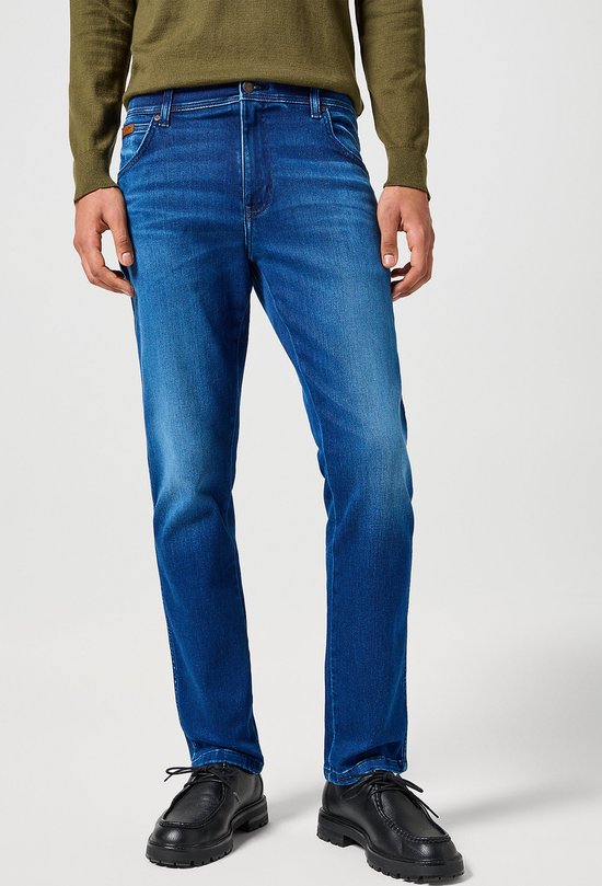 Model draagt slanke blauwe jeans met een licht vervaagd effect op de benen.