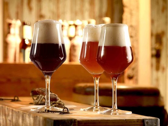 Drie glazen met donker en amberkleurig bier en schuimkoppen, geplaatst op een houten bar.