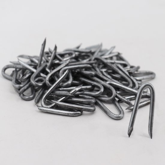 Une pile d'agrafes métalliques en forme de U avec des pointes acérées sur fond blanc.