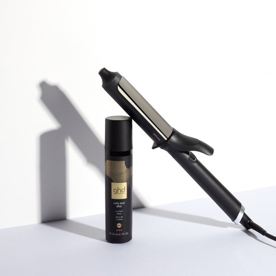Ghd Curve krultang naast een flesje met goudkleurige opdruk.