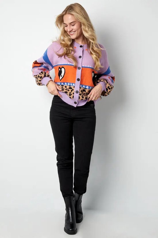 Vrouw met blonde haren, draagt paars vest met luipaardprint, hartjes en blauwe strepen.