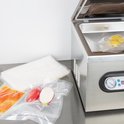 Roestvrijstalen vacuümmachine met open deksel, met een gele appel en groenten in vacuümzakken.