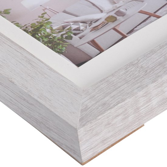 Detail van een lichte, houtnerf fotolijst met witte passe-partout en interieurfoto.