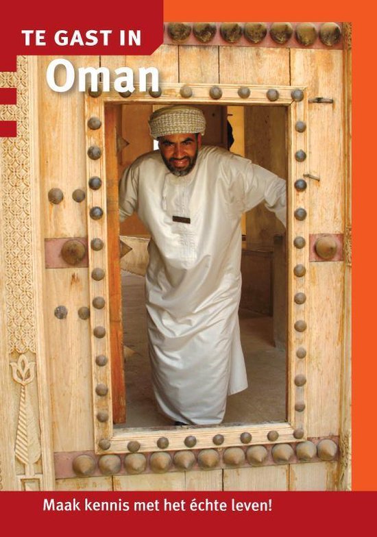 Man in traditioneel Oegandees gewaad, met een tulband, die door een houten deur kijkt. TE GAST IN Oman.
