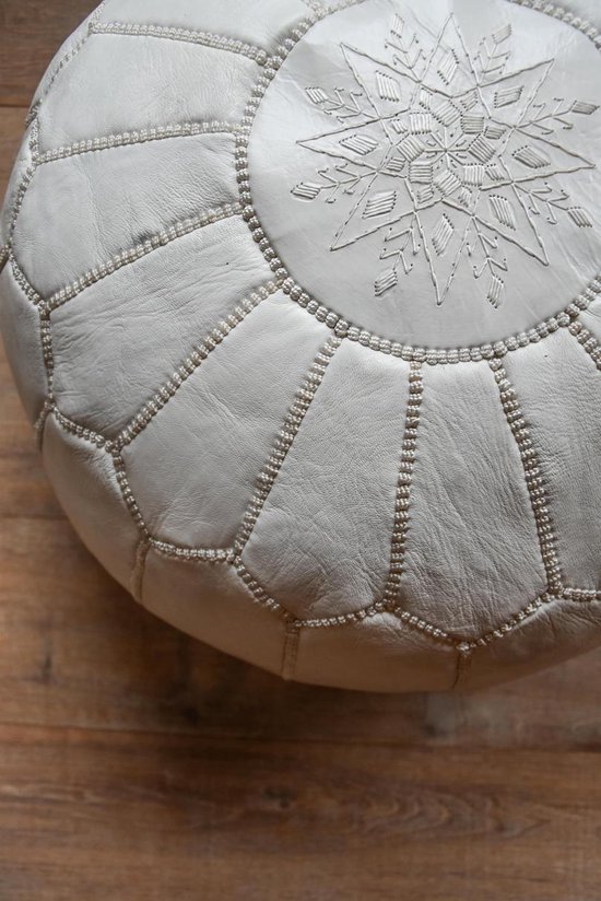 Gedetailleerd zicht op een ronde witte poef met strakke naden en een zilverkleurig, ster-achtig detail in het midden.