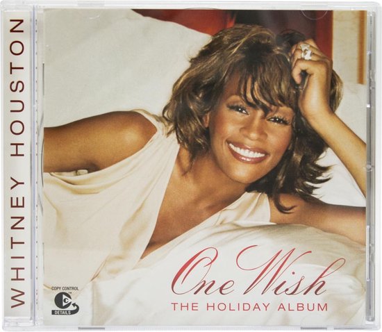 Whitney Houston met een brede glimlach, leunend op bed, op de albumhoes "One Wish: The Holiday Album".