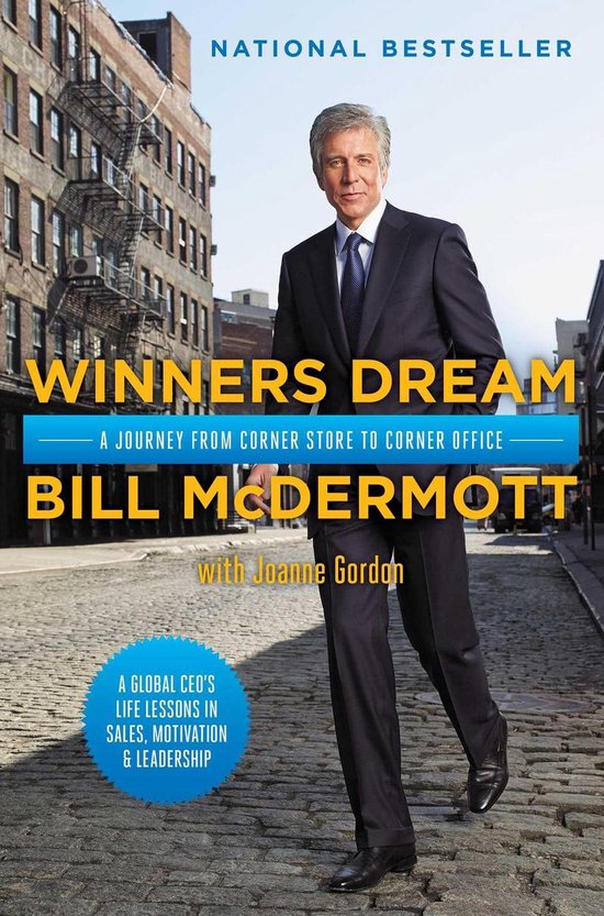 Bill McDermott, gekleed in een pak, op een stenen straat voor een gebouw.