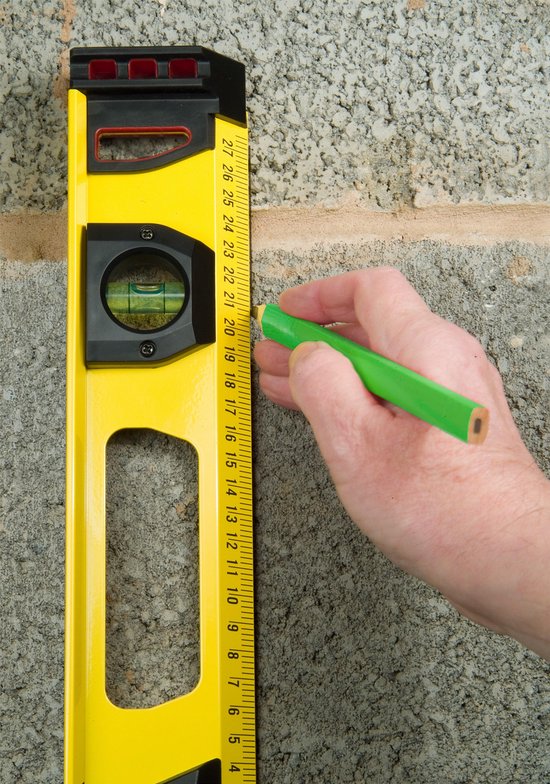 Hand met groen potlood markeert op gele Stanley FatMax waterpas tegen een stenen muur.
