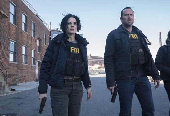 Man en vrouw met FBI-vesten en wapens, lopend in een stad.