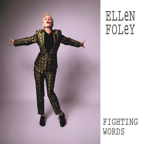 Ellen Foley in een zwart met gouden glitterprint colbert en bijpassende broek, met haar armen wijd open.
