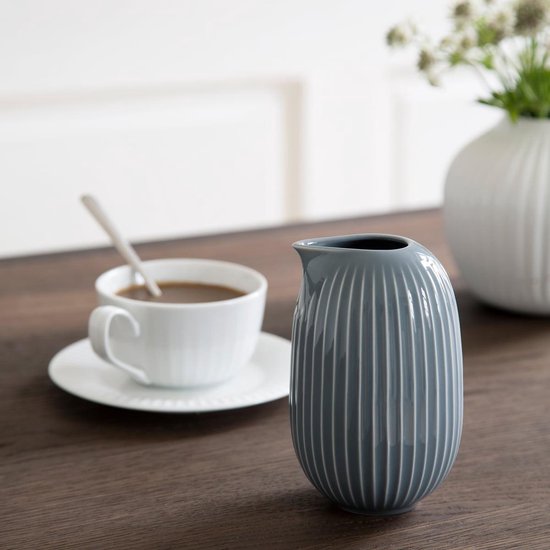 Grijze karaf met verticale ribbels op een houten tafel naast een kop koffie.