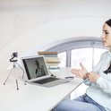Femme derrière un ordinateur portable, conversation par webcam, livres en arrière-plan.