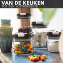 Doorzichtige voorraadpotten met zwarte deksels, gevuld met koffiebonen, koffiepads, snoepjes en suiker, naast kleurrijke mokken.