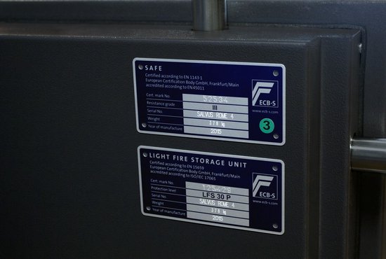 Close-up van certificeringsstickers op de deur van een grijze kluis.