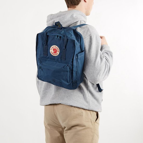 Man met marineblauwe Kånken rugzak op zijn rug, draagt een grijze hoodie.