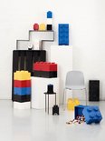 Stapel witte, zwarte, blauwe, gele en rode LEGO opbergdozen, een grijze stoel en een zwarte kruk.