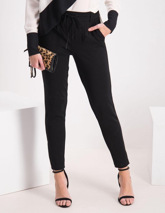 Model draagt zwarte broek met ceintuur en hoge hakken, met een dierenprint clutch.