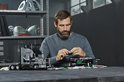 Man bouwt aan een LEGO Technic Mack Anthem truck. Hij houdt een klein rond onderdeel vast.