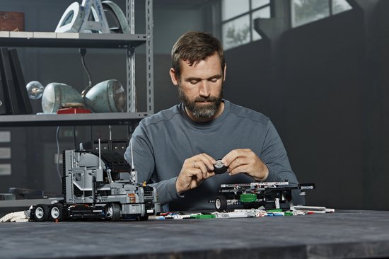 Man bouwt aan een LEGO Technic Mack Anthem truck. Hij houdt een klein rond onderdeel vast.