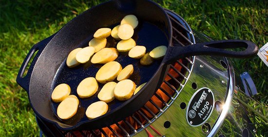 Gietijzeren pan met plakjes aardappel, op een grill van de 'Atago' met vlammen eronder.