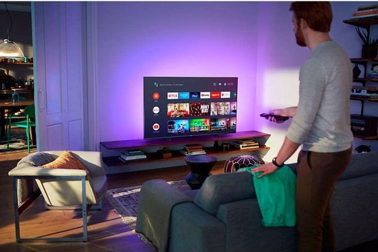 Man met rode baard met afstandsbediening voor een Philips tv in woonkamer met Ambilight.