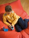 Jongen in geel shirt ligt op een rode zitzak, bezig met een blauwe DYMO Junior lettertang.