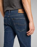 Achterkant van een man in donkerblauwe Lee jeans met bruin leren merklabel en kenmerkende stiksels op de zakken.