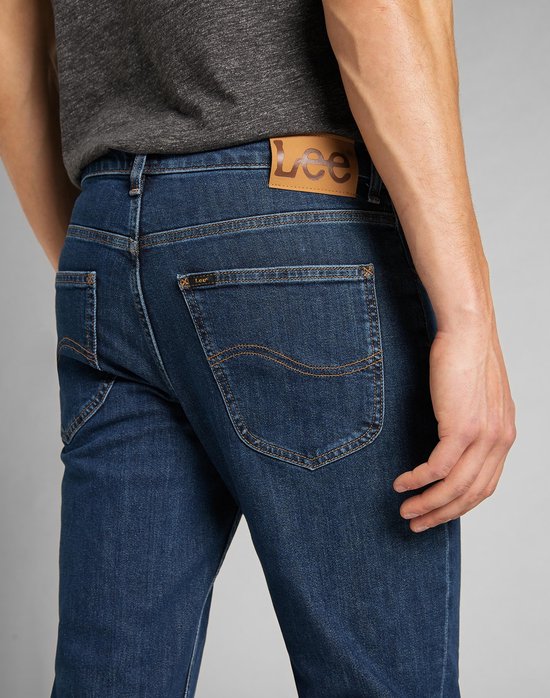 Achterkant van een man in donkerblauwe Lee jeans met bruin leren merklabel en kenmerkende stiksels op de zakken.