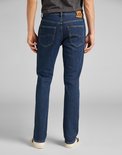 Achterkant van een man in donkerblauwe Lee jeans met rechte pasvorm, met bruin leren merklabel en stiksels.