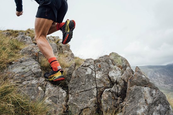 Jambes de coureurs en chaussettes Falke oranges et chaussures de trail, grimpant sur un terrain rocheux.