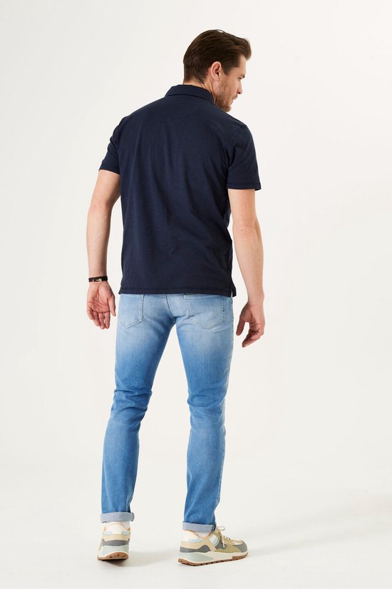 Man met donkerblauwe polo en lichtblauwe jeans, staand van achteren.