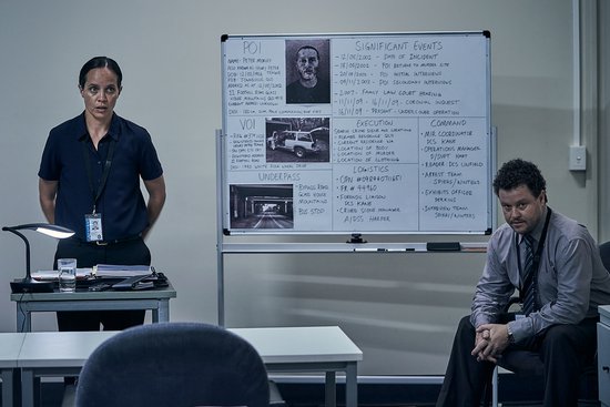 Een vrouw staat naast een whiteboard met aantekeningen, terwijl een man zit te midden van een kantooromgeving.