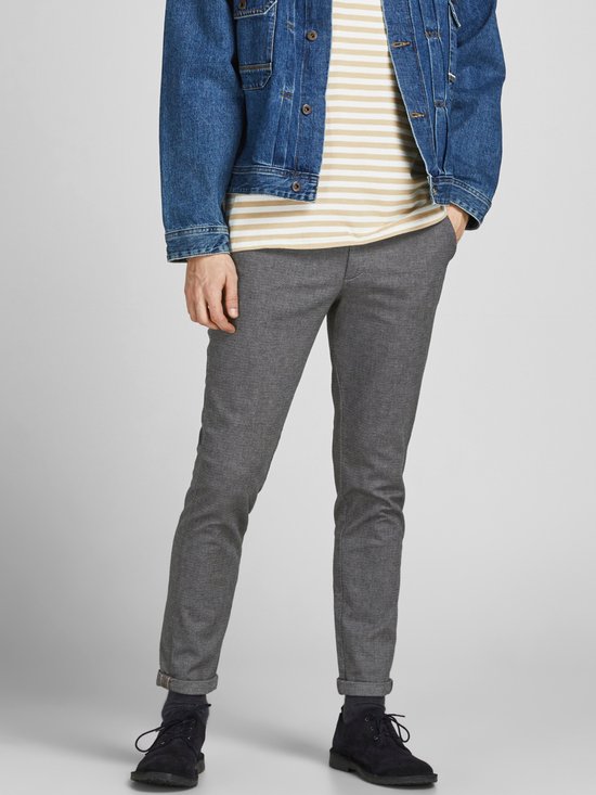 Model in grijze broek met visgraatpatroon, gestreepte top en spijkerjack.
