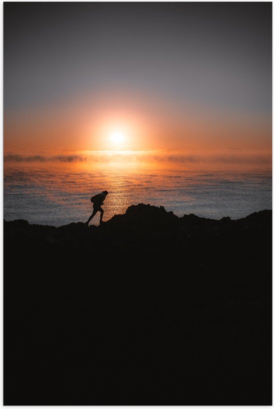 WallClassics - Poster Glanzend – Man lopend over Berg aan de Zee met Zonsondergang - 60x90 cm Foto op Posterpapier met Glanzende Afwerking