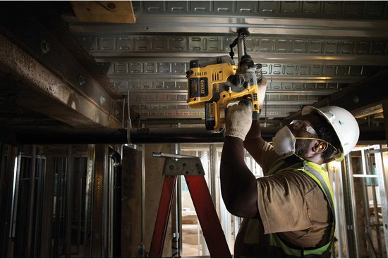 Man met helm en veiligheidsbril gebruikt een gele en zwarte DeWalt accuhamer om een gat te boren in een plafond.