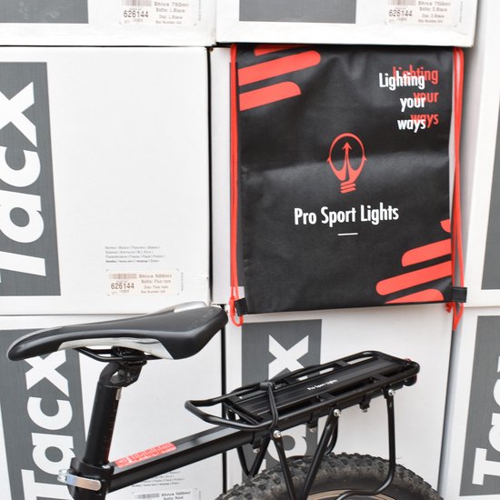 Zwarte fietsbagagedrager op een fiets, naast een zwarte tas met rode opdruk 'Lighting your ways'.