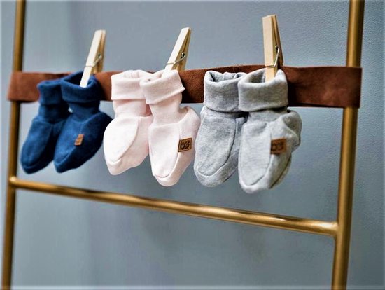Trois paires de chaussons pour bébé sont suspendues à une bande marron avec des pinces à linge. De gauche à droite : bleu foncé, rose pâle et gris.