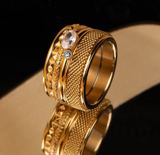 Bague dorée au design large et texturé, ornée d'une pierre claire et de deux petites pierres bleues.