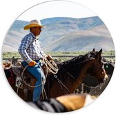 PVC Schuimplaat Muurcirkel - Cowboy op zijn Paard tussen Kudde bij Bergen - 70x70 cm Foto op Muurcirkel (met ophangsysteem)