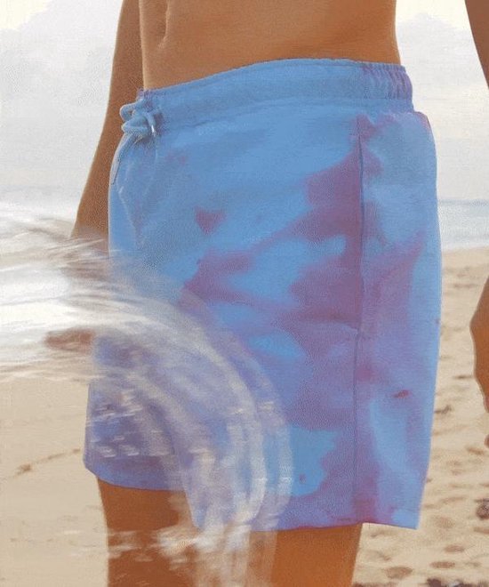 Close-up van een jongetje in een lichtblauwe en paarse zwembroek die in het water spettert op een strand.