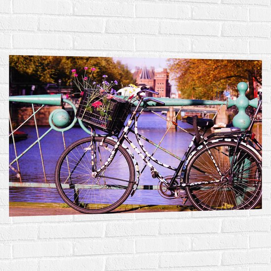 WallClassics - Muursticker - Zwarte bloementjes Fiets voor Blauw Hek bij het Water - 105x70 cm Foto op Muursticker