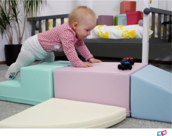 Un bébé joue avec des blocs de jeu souples aux couleurs pastel, y compris des marches bleu menthe et un bloc rose.
