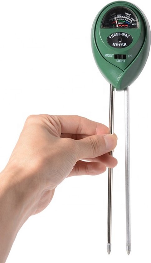 Hand die een groene driewegmeter vasthoudt met twee metalen sondes, op witte achtergrond.